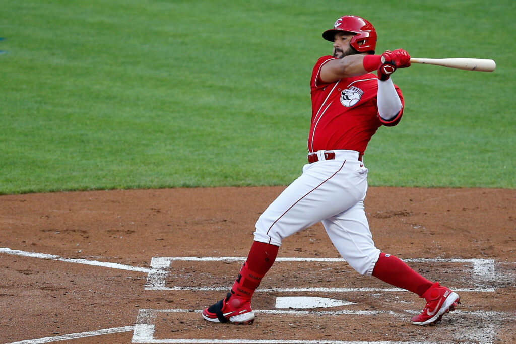 Eugenio Suárez mid swing in vibrant red uniform on lush baseball field with stadium energy background Wallpaper