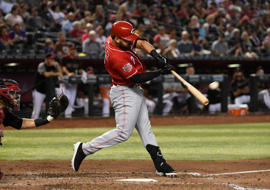 Eugenio Suárez mid-swing hitting baseball powerfully in red gray uniform on sunlit field stadium Wallpaper