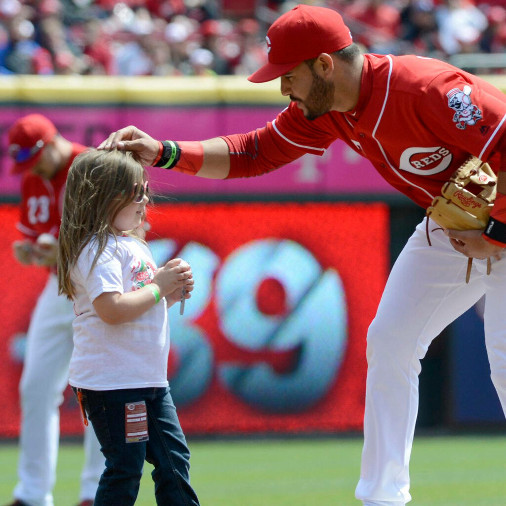 Eugenio Suárez in red Cincinnati Reds uniform gently pats little girl on head at baseball field Wallpaper