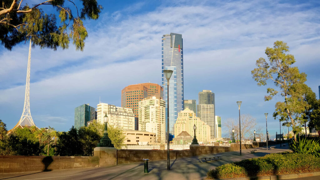 Eureka Tower with gold crown above Melbourne skyline blue glass modern buildings and green trees Wallpaper