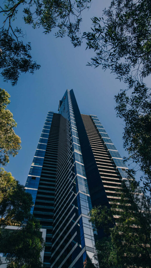 Eureka Tower Melbourne modern facade framed by green branches under clear blue sky wallpaper