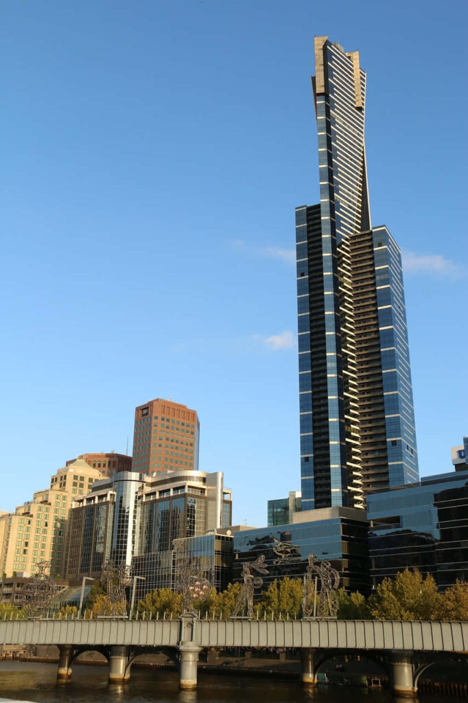 Eureka Tower Melbourne with modern glass facade gold accents city skyline riverside bridge background Wallpaper