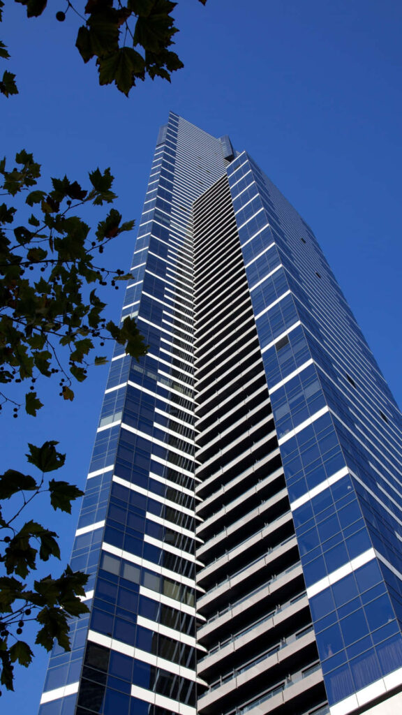 Eureka Tower Melbourne skyscraper with glass façade framed by green branches under blue sky wallpaper