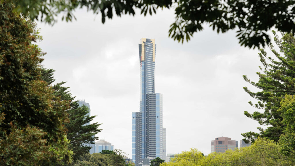 Eureka Tower Melbourne glass skyscraper with gold crown framed by lush greenery and cloudy sky Wallpaper