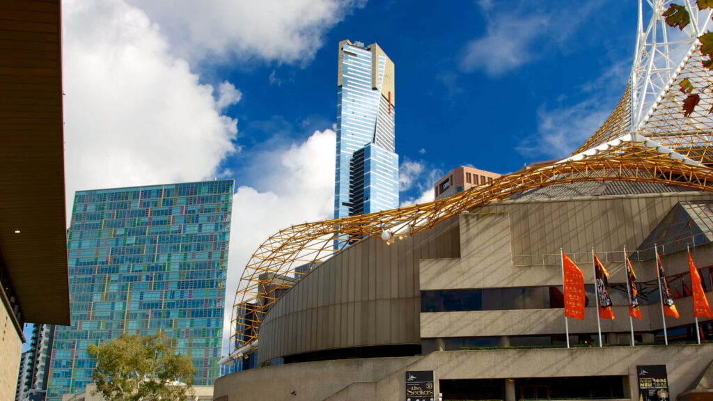 Eureka Tower soaring above Melbourne skyline with vibrant buildings and blue sky background Wallpaper