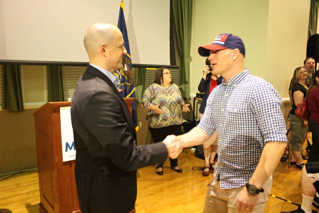 Evan McMullin shaking hands with supporter at political event with American flag backdrop Wallpaper