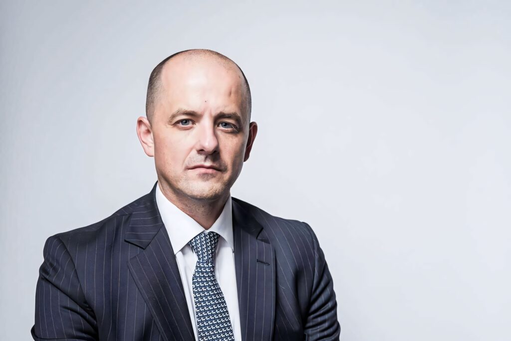 Evan McMullin professional portrait in dark pinstripe suit and patterned tie on gray background Wallpaper