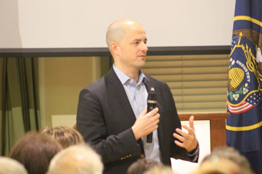 Evan McMullin speaking at public event wearing dark blazer light blue shirt with state flag background Wallpaper