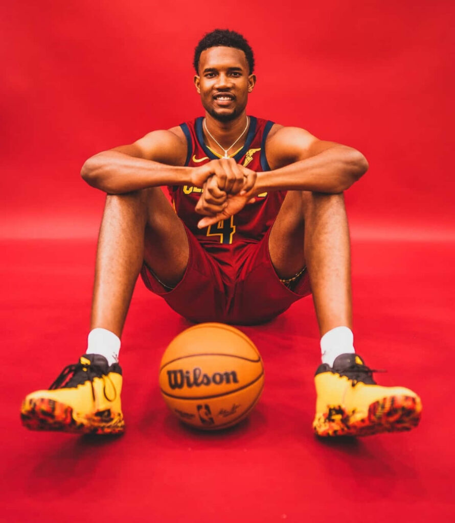 Evan Mobley in Cleveland Cavaliers uniform seated with basketball vibrant red sports portrait background Wallpaper