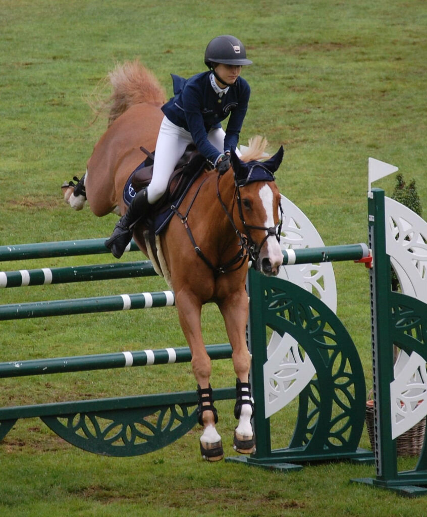 Eve Jobs expertly jumps green white fence in equestrian event wearing classic riding attire on grass Wallpaper