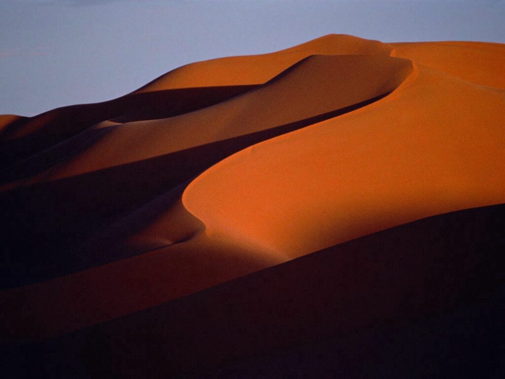 Desert wallpaper with warm evening light on sand dunes and distant mountains creating shadows