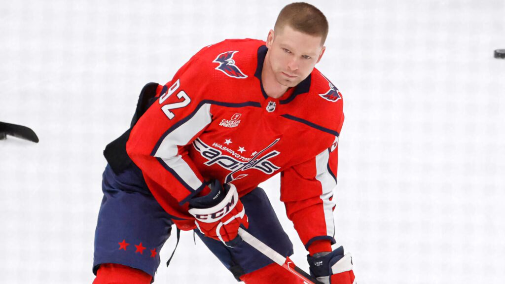 Evgeny Kuznetsov in red Washington Capitals uniform focused during hockey game on ice background Wallpaper
