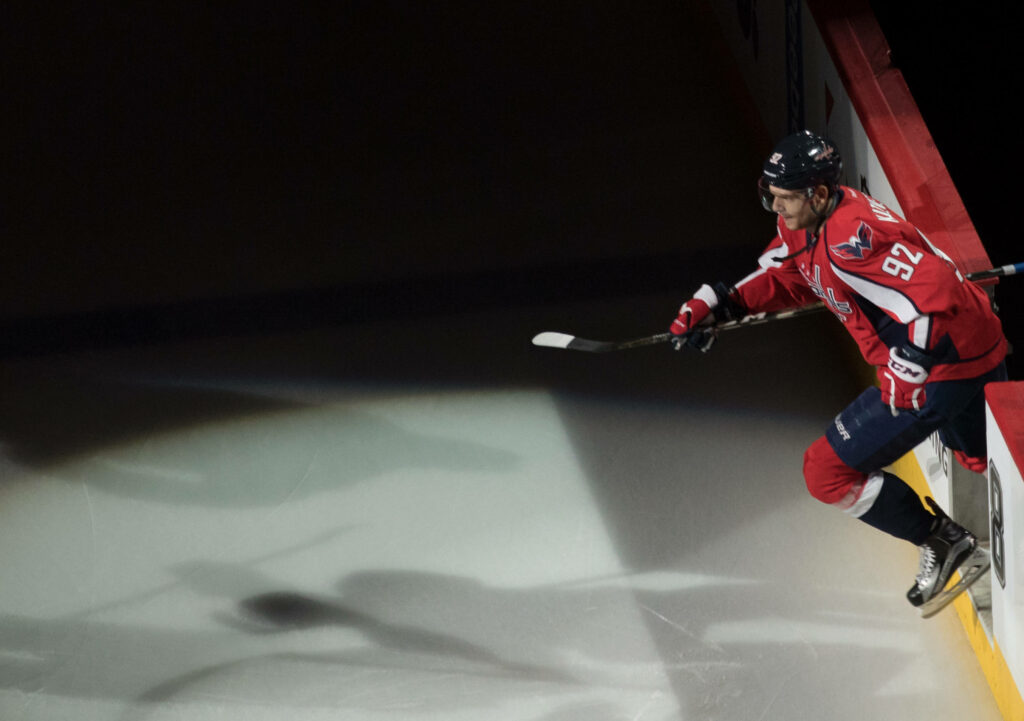 Evgeny Kuznetsov in Washington Capitals uniform leaping on ice with dynamic pose and dramatic lighting Wallpaper