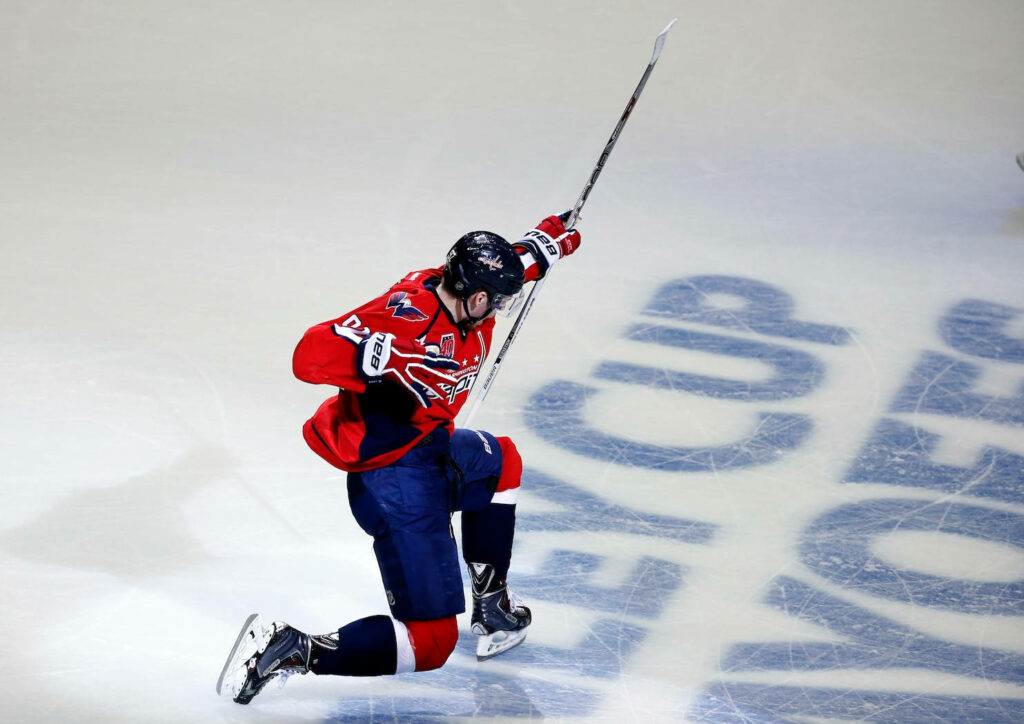 Evgeny Kuznetsov in red Capitals uniform celebrates dynamic hockey move under bright arena lights Wallpaper