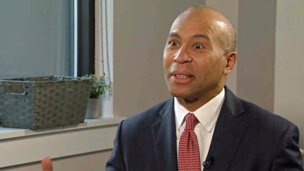 Ex-Governor Deval Patrick in dark suit and red tie speaking in well-lit office with wallpaper backdrop