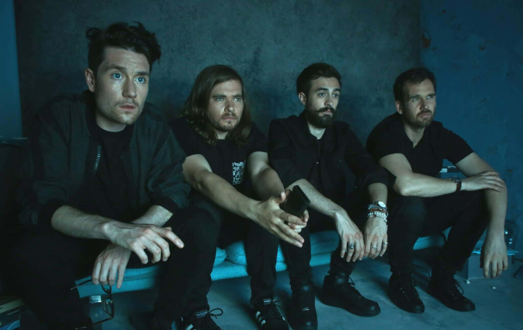 Experience the Freedom of Bastille band members sitting together in moody blue-toned setting wallpaper