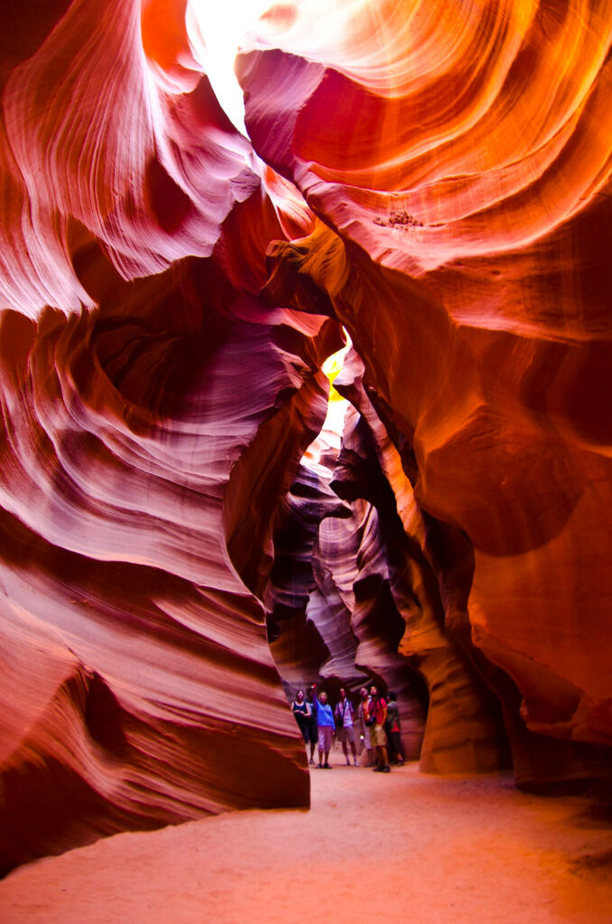 Tourists explore vibrant sunlit red and orange sandstone walls in Antelope Canyon passageways Wallpaper