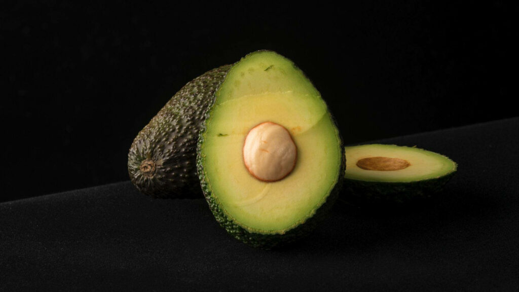 Captivating Close-up: A Large Avocado Slice with Intact Seed on Black Background Wallpaper