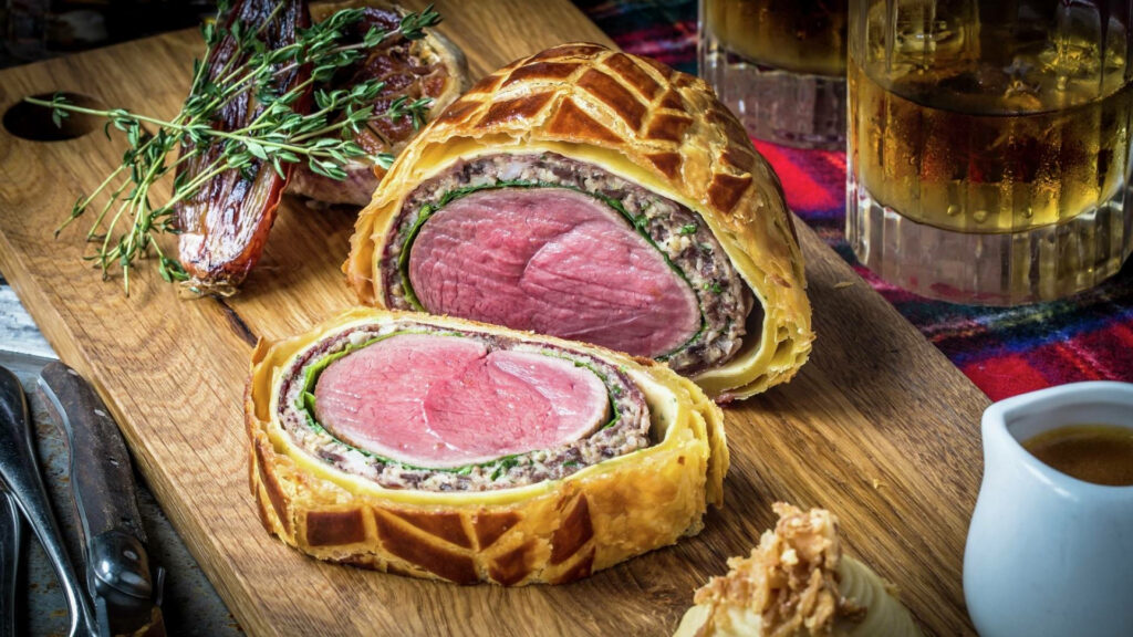 Beef Wellington with golden flaky pastry fresh herbs and gourmet sides culinary wallpaper background