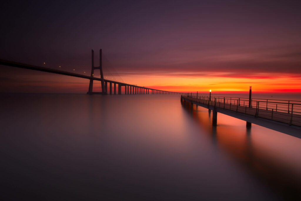 Majestic Sunset: The Tranquil Vasco Da Gama Bridge Amidst Portugal's Misty Coastal Splendor Wallpaper