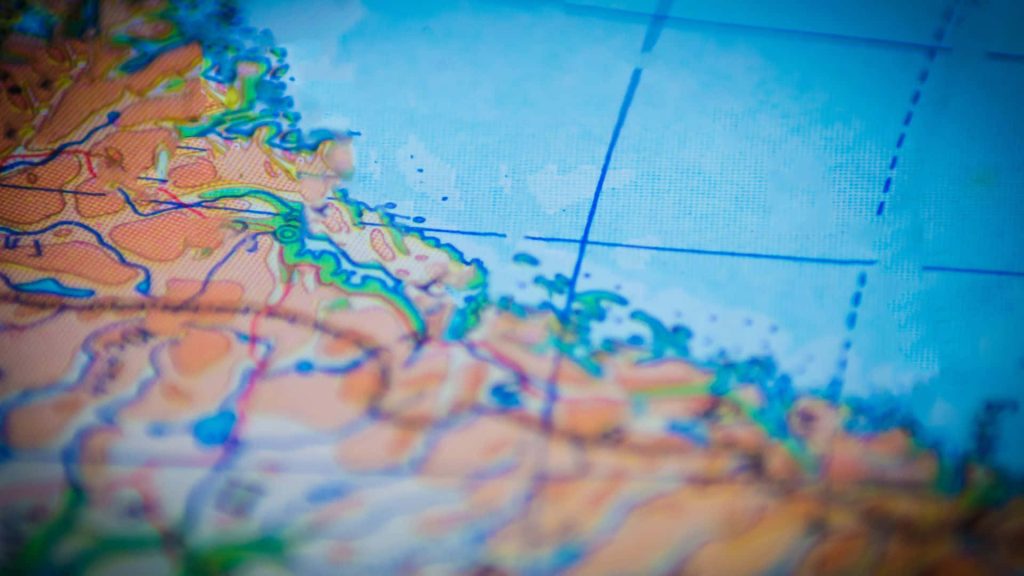 Extreme close-up of a detailed physical map showing coastline with grid lines and vibrant colors Wallpaper