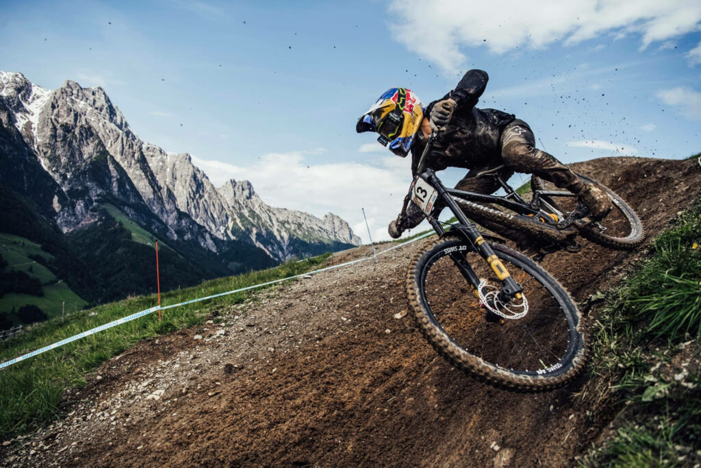 Cyclist speeding down rugged Leogang downhill track with alpine peaks and vivid blue sky Wallpaper