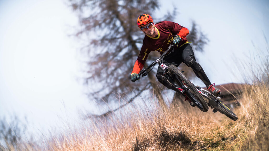 Extreme cyclist riding mountain bike through tall golden grass under clear blue sky outdoors Wallpaper
