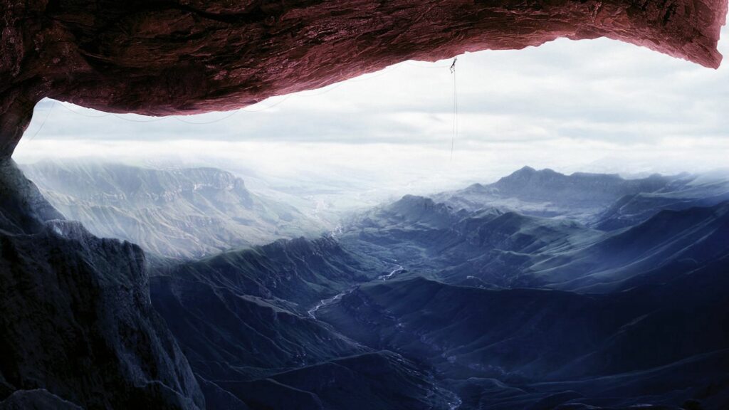 Climber hanging from steep rock overhang above misty mountain ridges adventurous outdoor scene Wallpaper