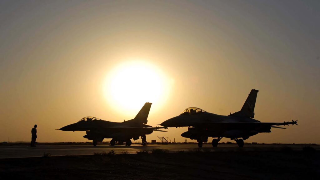 Silhouetted F-16 Fighting Falcon jets on tarmac at sunset showcasing military power and elegance Wallpaper