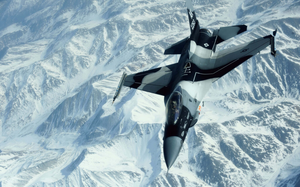 General Dynamics F-16 Fighting Falcon flying over snow-covered rugged mountains aviation wallpaper