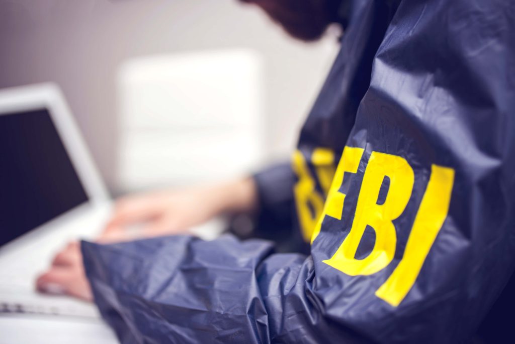 Person in FBI navy jacket typing on laptop with bold yellow FBI logo visible on sleeve Wallpaper