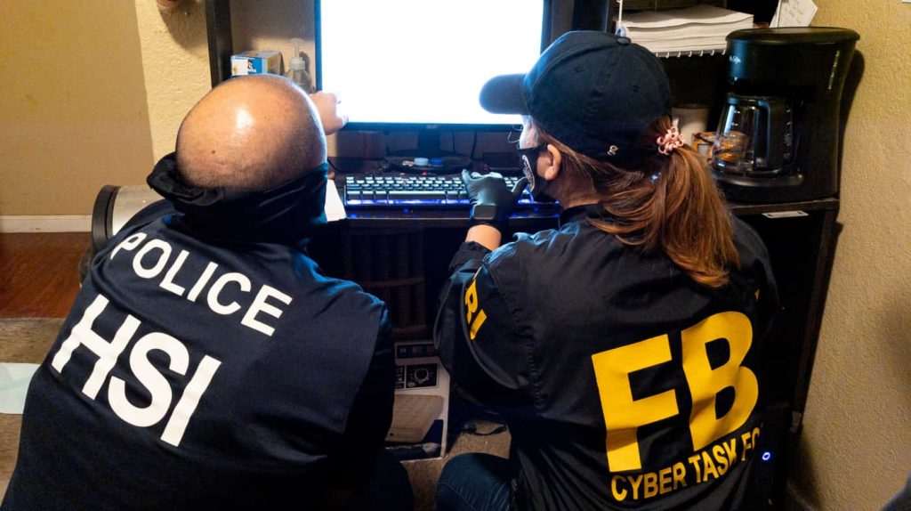 HSI agent and FBI Cyber Task Force officer collaborate in dim office analyzing digital evidence wallpaper