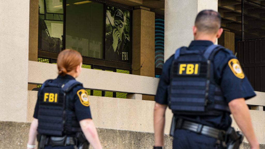 Two FBI agents in tactical gear patrol outside FBI headquarters with negotiator sign visible Wallpaper