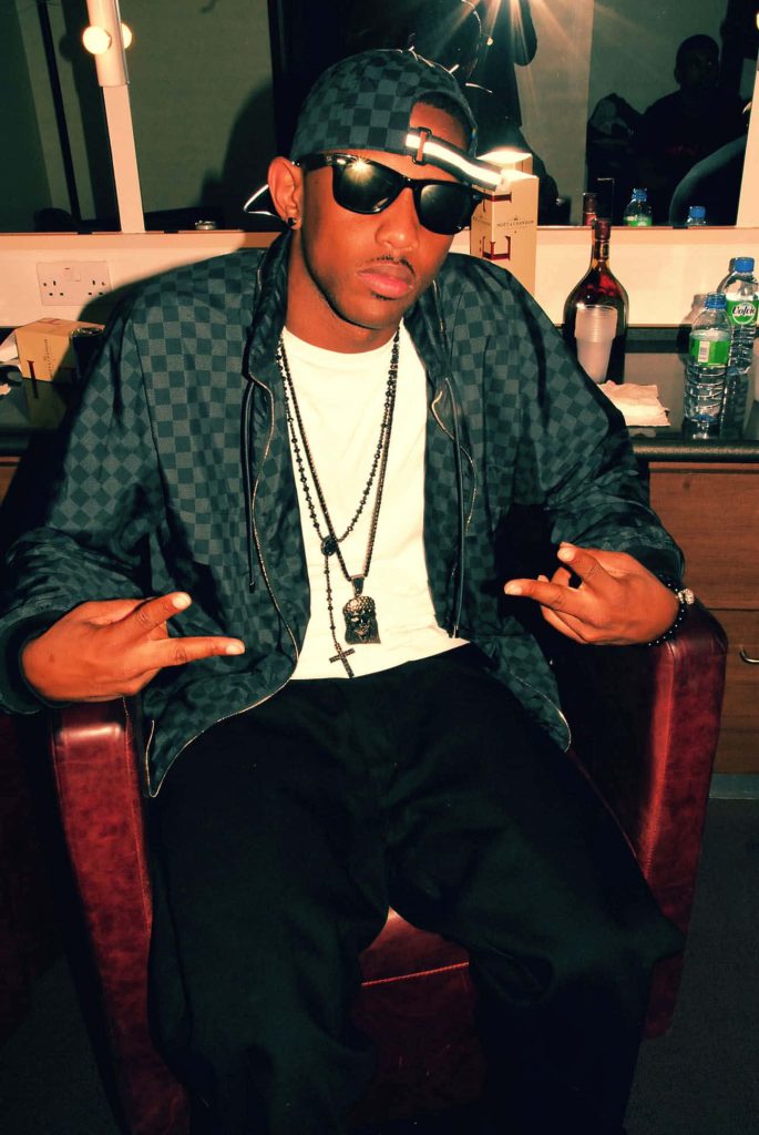 Fabolous rapper relaxing backstage in red chair wearing checkered jacket cap and sunglasses Wallpaper