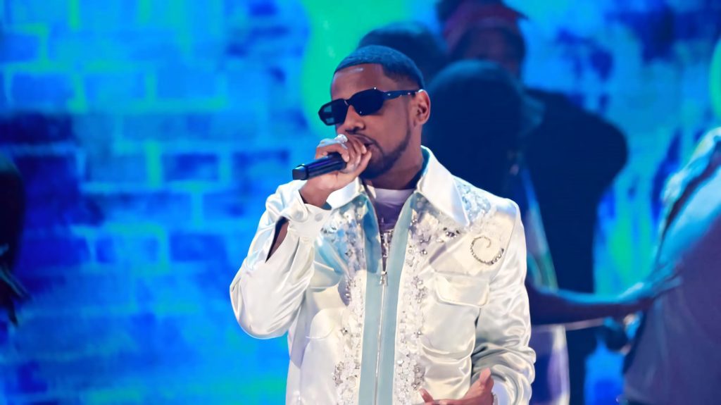 Rapper Fabolous live performing in white satin jacket with silver details on blue lit stage Wallpaper