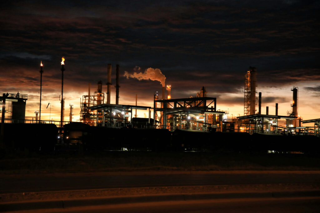 Factory at dusk with glowing lights fiery chimneys and dramatic blue orange industrial sky background Wallpaper