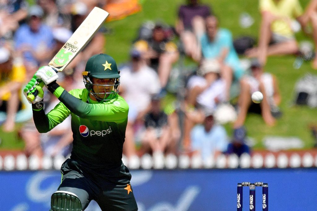 Pakistani cricketer Fakhar Zaman batting mid-swing in green kit with NZC stumps background Wallpaper
