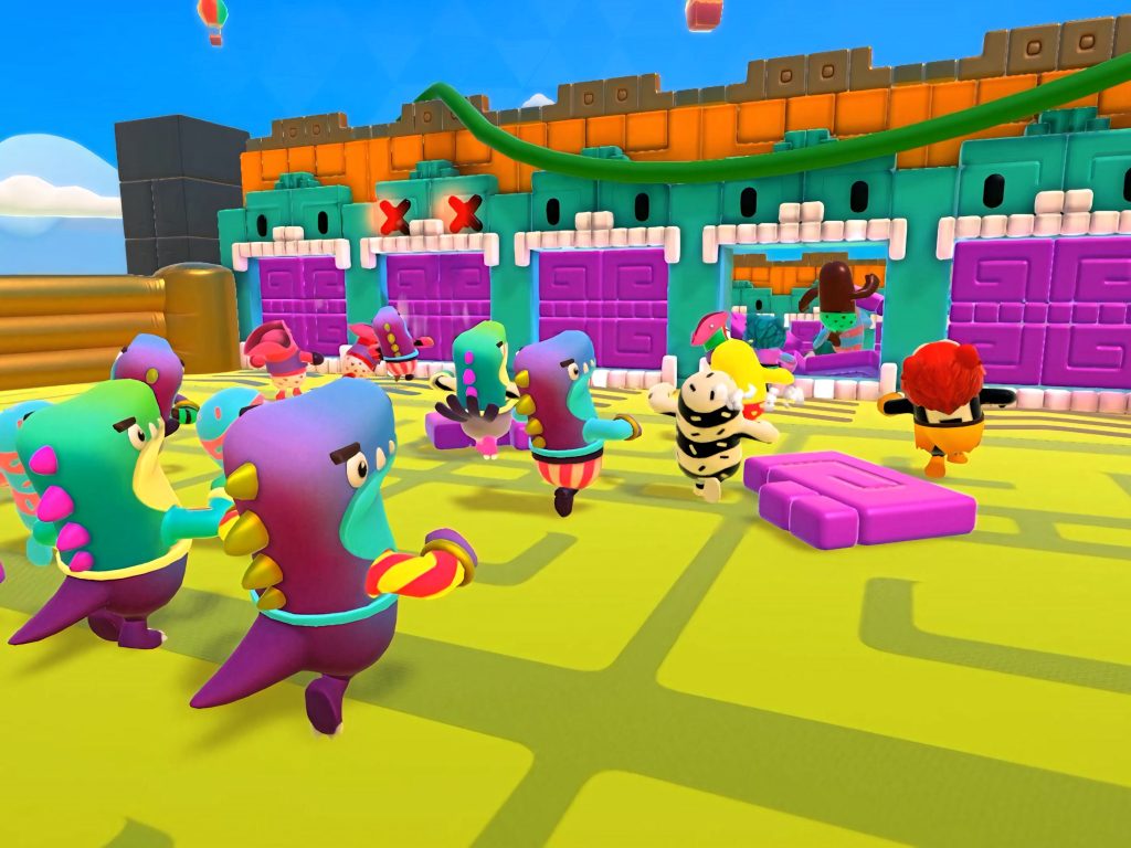 Colorful Fall Guys characters race in a bright yellow arena with purple doors under blue sky Wallpaper