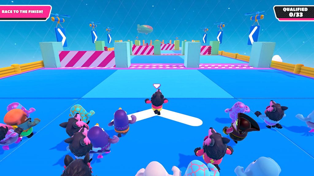 Fall Guys characters race in colorful costumes across a bright blue arena toward barricades Wallpaper