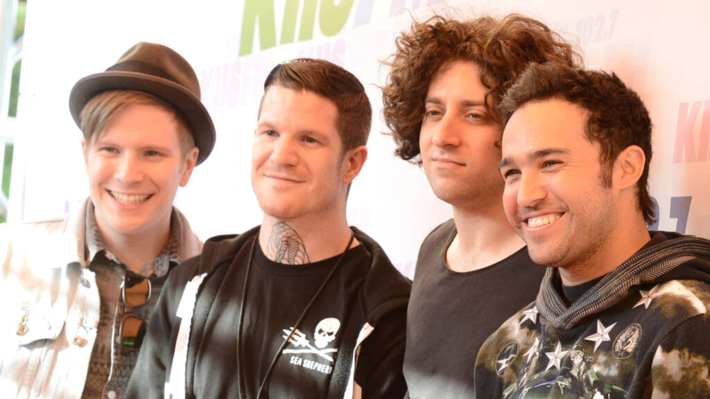 Fall Out Boy band smiling under spotlight energetic iconic rock group wallpaper background