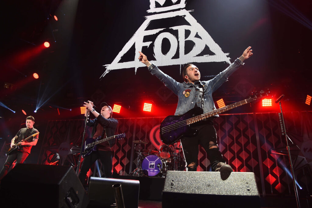 Fall Out Boy live concert energetic performance with illuminated FB logo on stage background Wallpaper