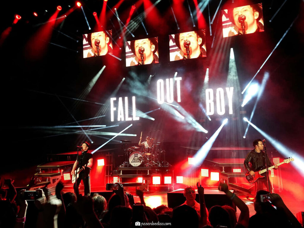 Fall Out Boy performing live under vibrant lights with illuminated band name and fans capturing moments Wallpaper