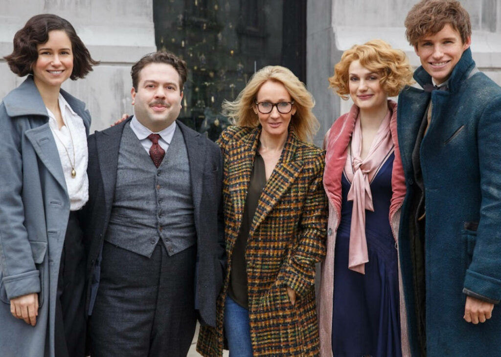 Fantastic Beasts cast and JK Rowling smiling in stylish outfits with urban wallpaper background