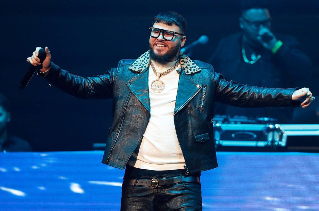 Reggaeton artist Farruko performing live in leather jacket with gold jewelry vibrant stage background Wallpaper