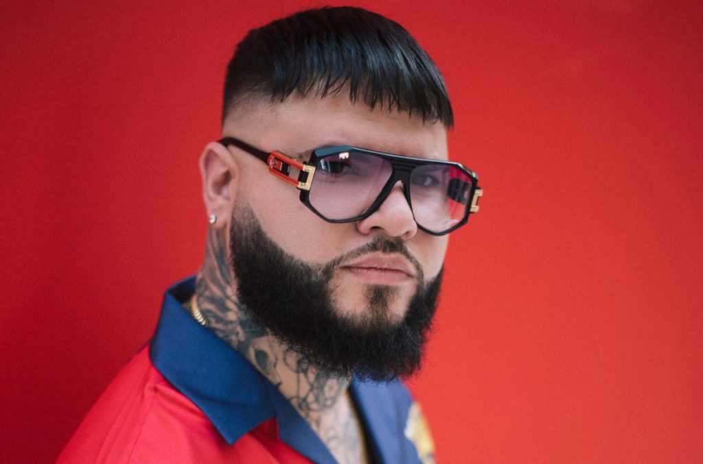 Bold portrait of reggaeton star Farruko in oversized sunglasses with red blue shirt and tattoos Wallpaper