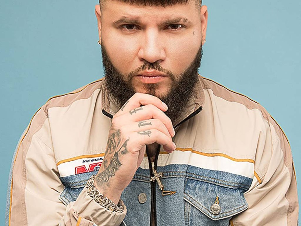 Farruko intense gaze portrait with tattoos cross necklace beige denim jacket blue background Wallpaper