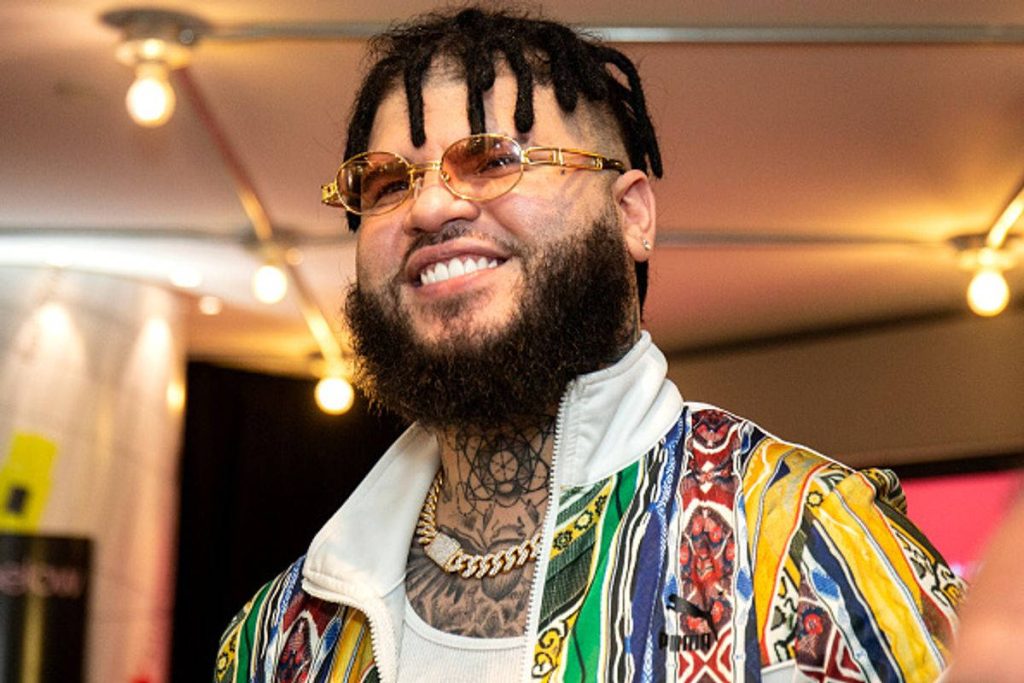Farruko portrait in colorful jacket dreadlocks gold chain neck tattoos warm indoor lighting wallpaper