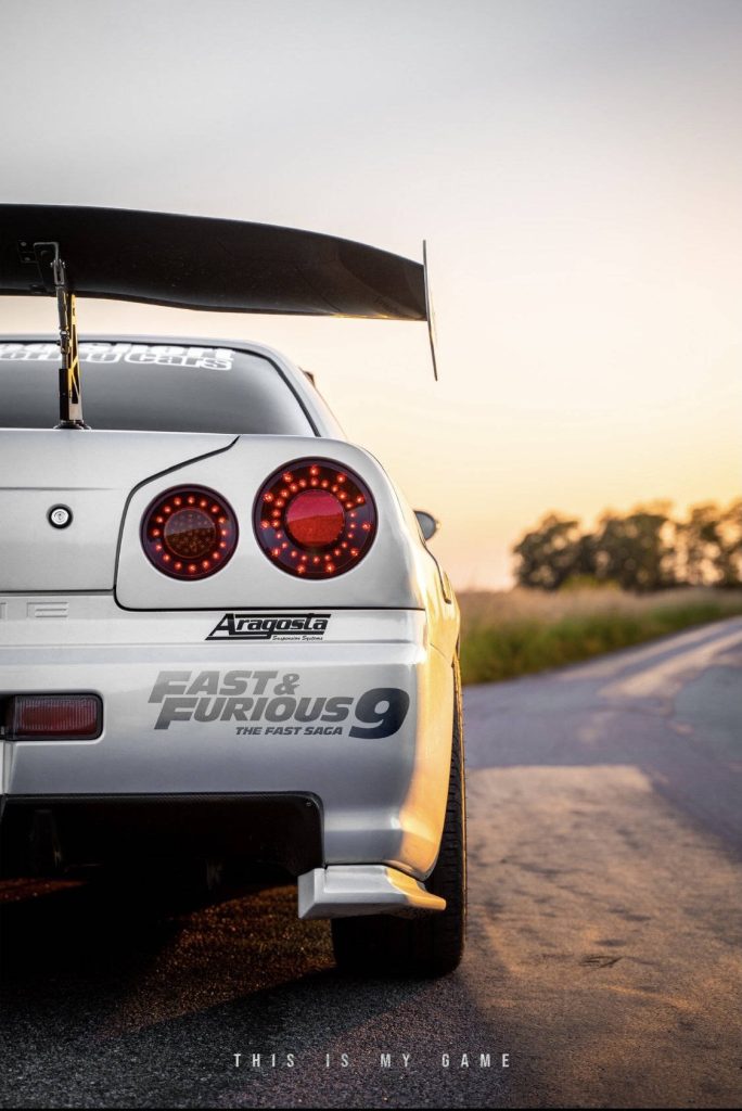Cinematic silver sports car rear with round red taillights and Fast Furious 9 decal at sunset Wallpaper