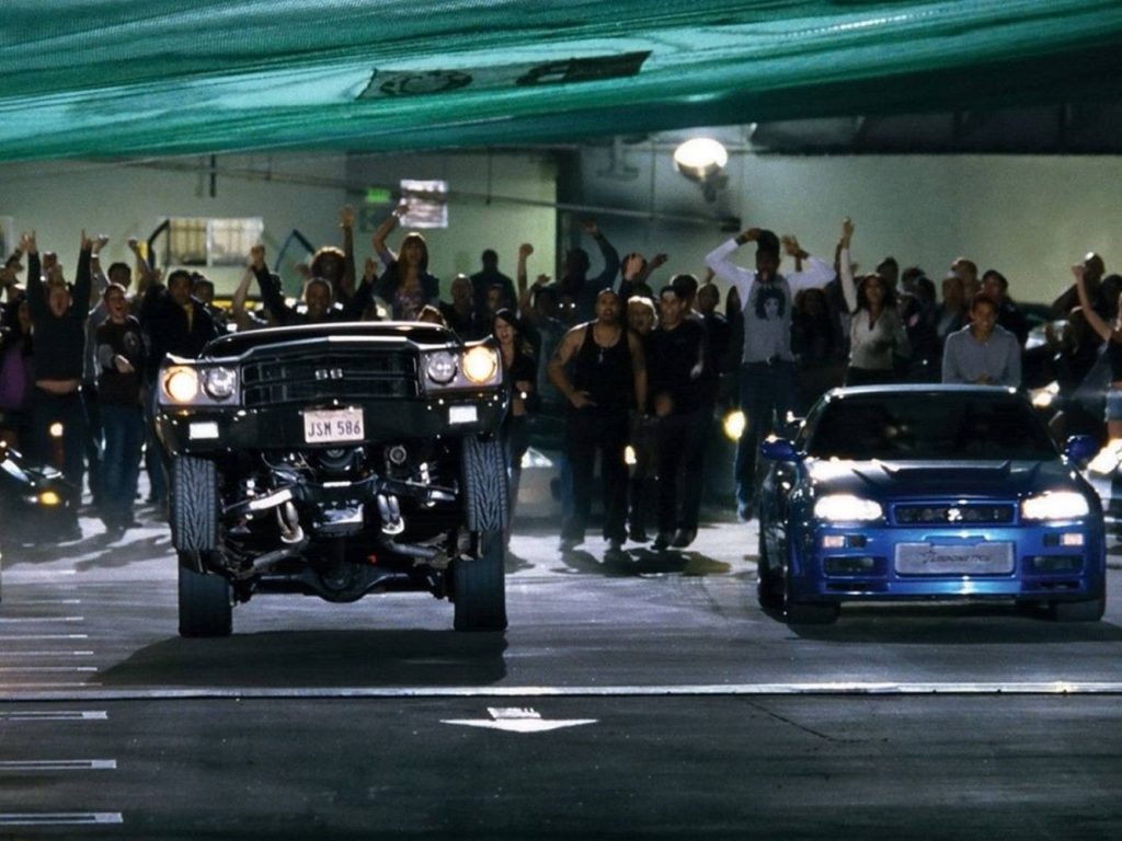 Black muscle car wheelie vs blue Nissan Skyline GT-R R34 in intense night street race wallpaper