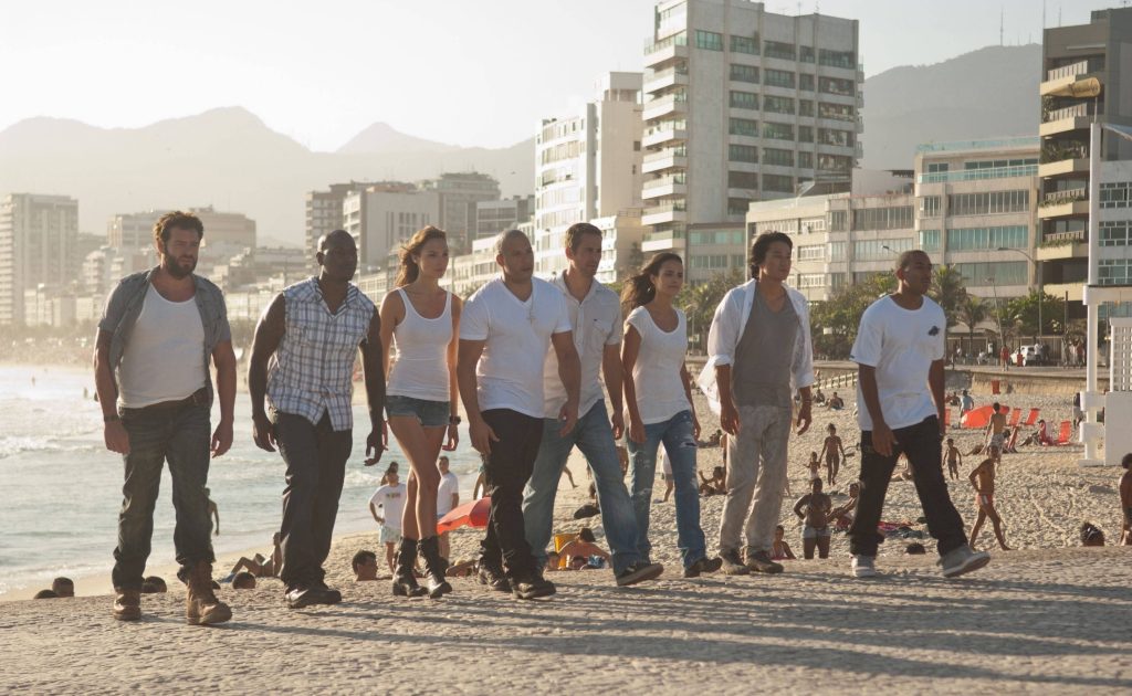Fast and the Furious cast Vin Diesel Paul Walker walking on sunlit beach promenade coastal view Wallpaper